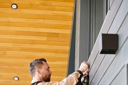 Técnico em uma escada instalando um equipamento na fachada de um prédio (foto de banco de imagens)