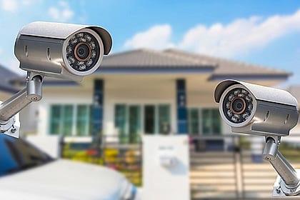 Duas câmeras de CFTV em primeiro plano com uma casa desfocada ao fundo