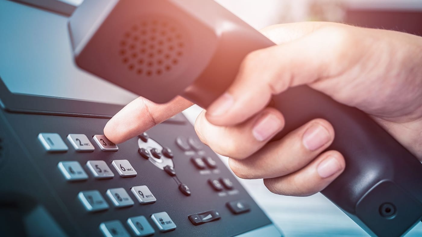 Uma mão levanta o monofone de um telefone IP de mesa